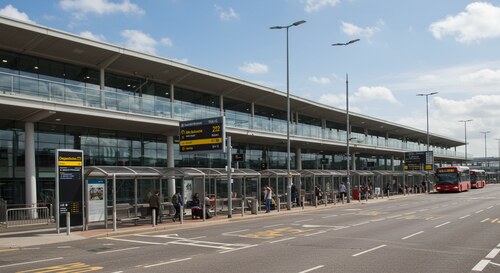 Luton Airport terminal building exterior with bus stop area and clear signage showing arrivals and departures
